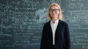 Smiling female teacher in front of chalkboard with complex equations.